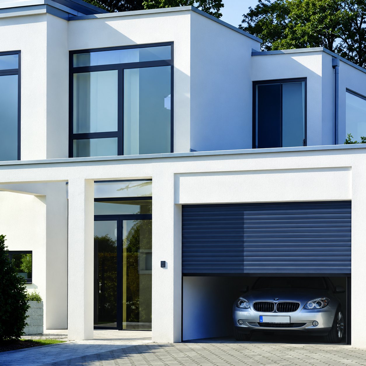 Façade d'une maison contemporaine blanche avec grandes baies vitrées et un garage ouvert à volet roulant bleu abritant une voiture grise.